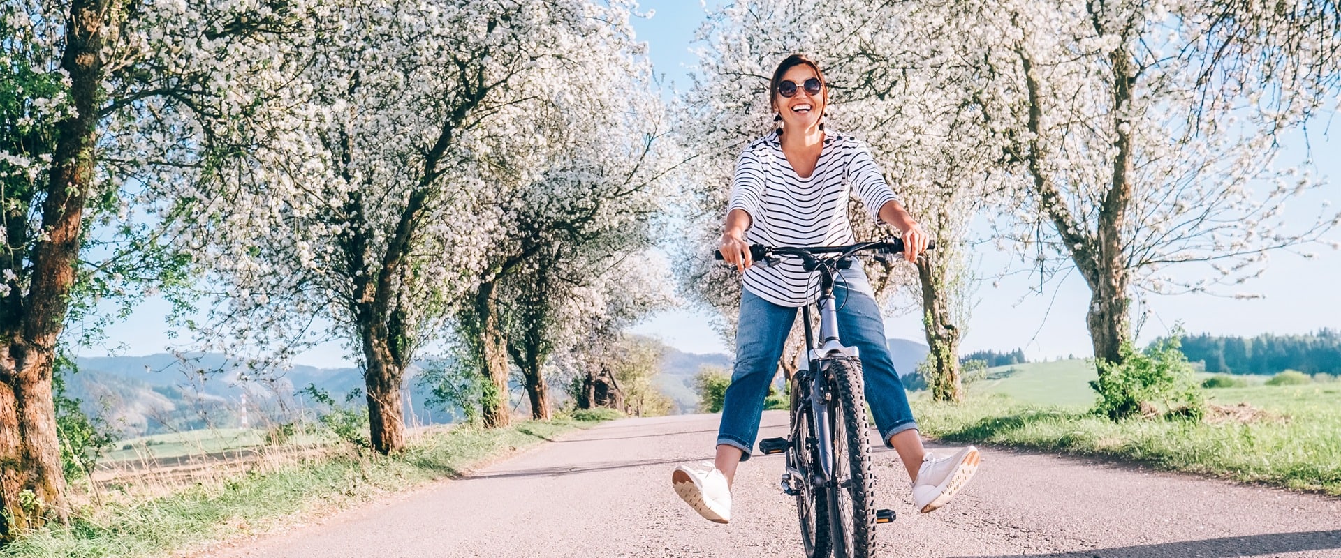 Happy smiling woman rides a bicycle on the country road under the apple blossom trees